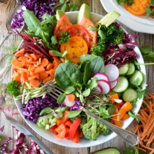 Une appétissante salade de crudités avec radis, concombre, carottes râpées, chou rouge, brocolis, tomates, avocats, courgettes, betteraves, jeunes pousses, mâche, et des brins de persil.