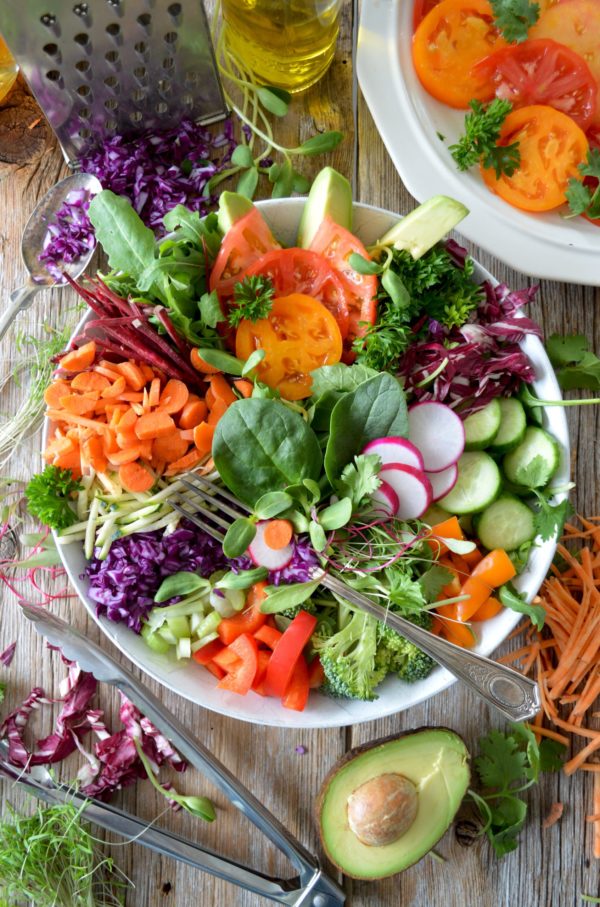 Une appétissante salade de crudités avec radis, concombre, carottes râpées, chou rouge, brocolis, tomates, avocats, courgettes, betteraves, jeunes pousses, mâche, et des brins de persil.
