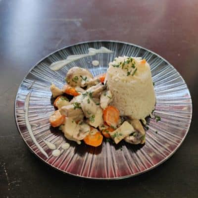 Une belle assiette d'une blanquette de poulet avec sa sauce, ses légumes et du riz.
