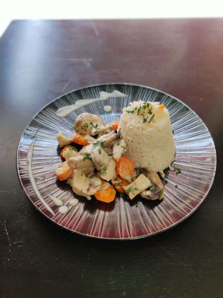 Une belle assiette d'une blanquette de poulet avec sa sauce, ses légumes et du riz.